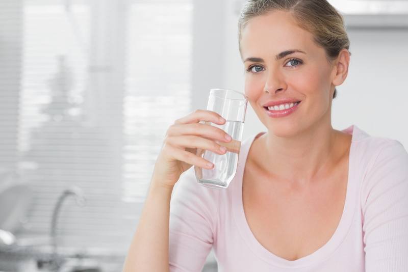 Beautiful woman drinking a glass of pure drinking water in her kitchen